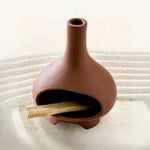 Un brûleur d'encens pour Palo Santo en céramique couleur terre cuite posé sur du sable fin