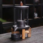 Un Brûleur d’encens à reflux en céramique & verre avec support bois posé sur une table en bois noir