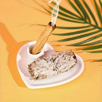 Photo d'Un Brûleur de Palo Santo et Sauge en Céramique en Forme de Cœur avec un baton de palo santo et de la sauge allumée