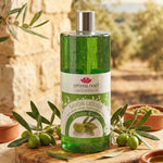 Un savon liquide à l'huile d'olive de la marque Emma Noel accompagné d'olives de part et d'autre du produit. Le produit est dans un environnement extérieur provençal.