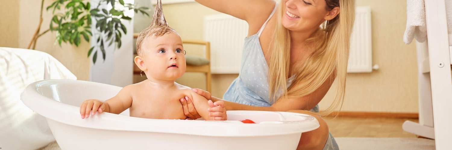 Un bébé dans un bain avec sa maman à côté qui s'amuse avec ses cheveux