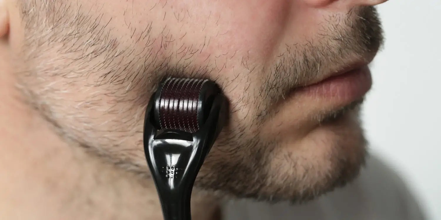 Gros plan sur un homme appliquant un dermaroller sur une zone clairsemée de sa barbe, concentré sur les joues