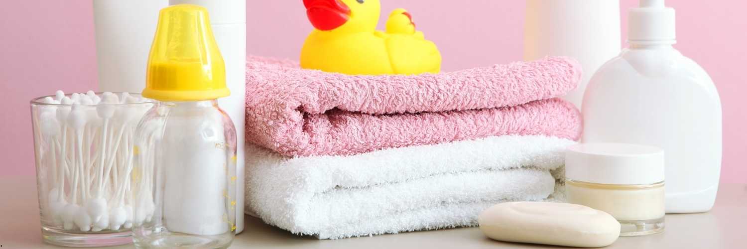 Photo d'un savon, de serviettes, un jouet pour bain en plastique et coton tige posées sur un meuble de salle de bain