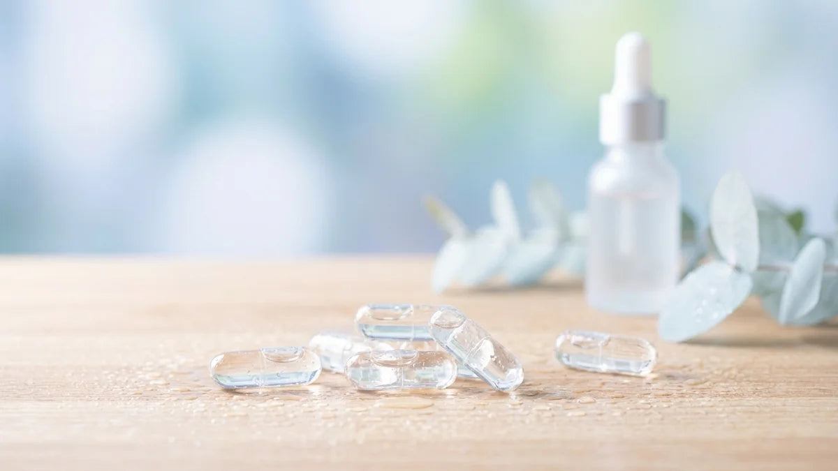 Gélules d'acide hyaluronique transparentes sur surface en bois avec gouttes d'eau