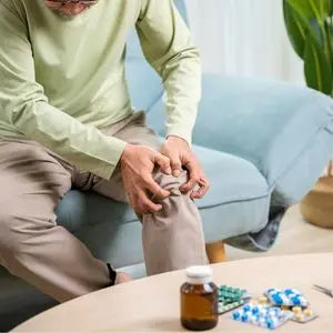 Homme âgé se tenant le genou douloureux, compléments alimentaires posés sur la table
