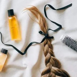 Tresse de cheveux nouée d'un ruban noir, à côté d'un flacon d'huile et d'une brosse