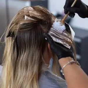 Coiffeuse appliquant une coloration végétale au pinceau sur des mèches