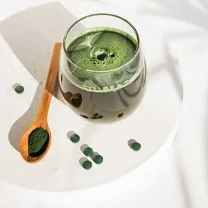 Boisson verte, comprimés de spiruline et cuillère de poudre sur une table blanche