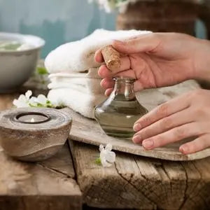 Main ouvrant un flacon d'eau florale en verre, à côté de serviettes et d'une bougie