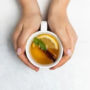 Mains tenant une tasse de tisane au citron et à la cannelle