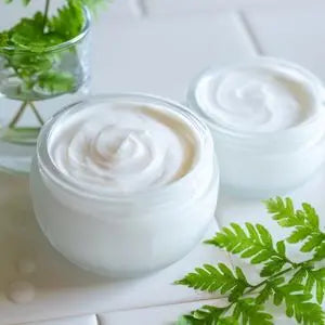 Pots de crème hydratante ouverts à la texture fondante, avec des feuilles de fougère