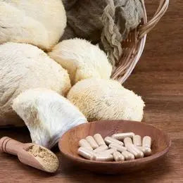 Des gélules de compléments alimentaires disposés dans une coupelle en bois au premier plan, avec à l'arrière plan des champignons Lion's Mane