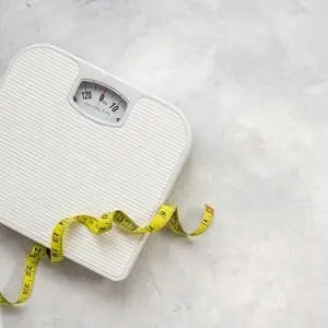 Pèse-personne blanc et mètre ruban jaune sur fond clair