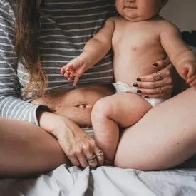 Photo d'une mère venant d'accoucher avec son bébé dans les bras, et ayant encore les marques physiques de l'accouchement sur son ventre