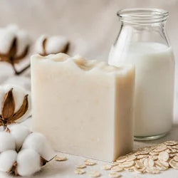 Savon au lait d'ânesse à côté d'une bouteille de lait, de fleurs de coton et de flocons d'avoine