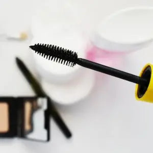 Brosse de mascara noir au premier plan devant une palette de maquillage