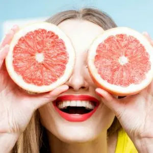 Femme souriante tenant deux moitiés de pamplemousse devant ses yeux