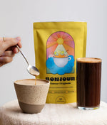 Une tasse de Bonjour Drink à côté drun sachet de Super Café aux champignons adaptogènes Saveur Originale