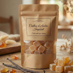 Photographie d'ambiance chaleureuse présentant un sachet artisanal de cubes d'ambre parfumés. Le sachet possède une fenêtre transparente laissant voir les cubes. 