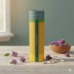 Flacon jaune et vert de Gomphrena, entouré de gélules blanches et de fleurs mauves sur une table en bois.