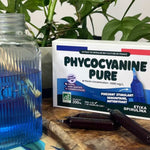 Une boite de phycocyanine pure de la marque Erika Spirulina en format ampoules. Les ampoules apparaissent devant la boite du produit. Des feuilles sont présentes en arrière plan.