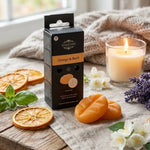 Packaging de la cire parfumée posé sur une table en bois entouré d'orange et de basilic.