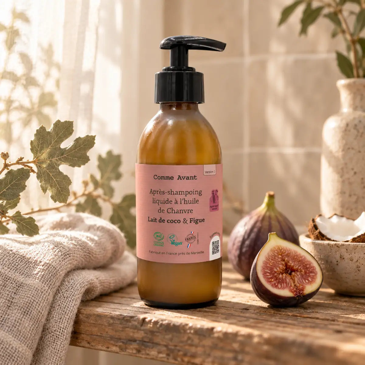 Flacon pompe ambré d'après-shampoing à l'huile de chanvre, lait de coco et figue, sur une étagère en bois avec serviette en lin et figue fraîche