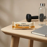 Barre Protéinée Caramel Humble+ sur un bureau avec haltère et bouteille d'eau