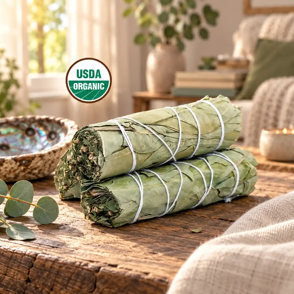 Bâtonnets de sauge blanche et eucalyptus biologiques, liés, posés sur une table en bois à côté d'une coupelle en céramique