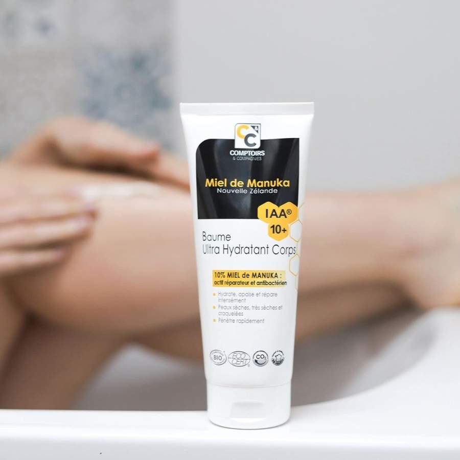 Un baume ultra hydratant bio au miel de Manuka Iaa10+ de 200 ml de la marque Comptoirs et compagnies devant une jambe