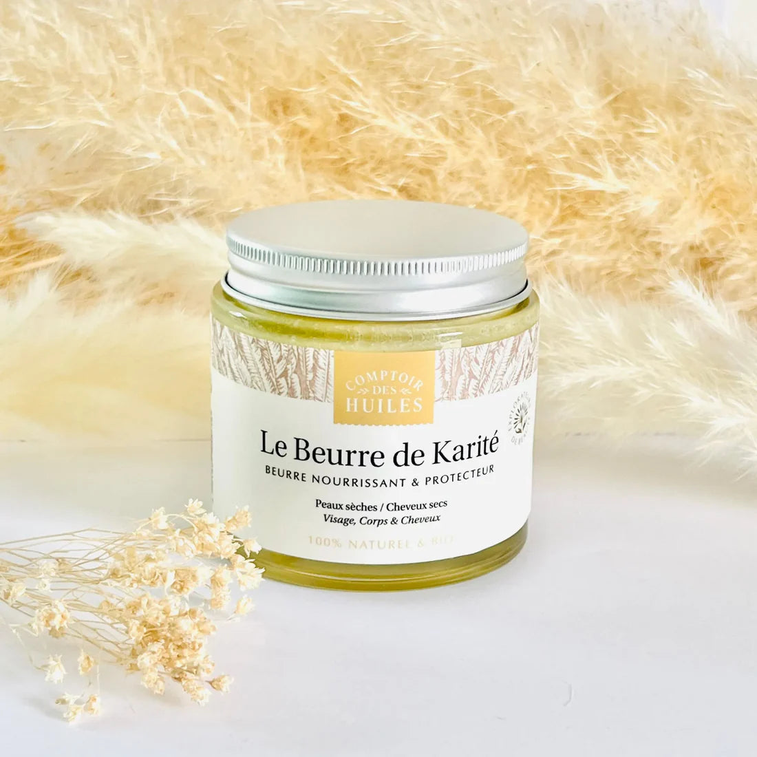 Un pot de beurre de Karité de 100 ml de la marque Comptoir des Huiles mis en scène sur une table avec des jolis fleurs