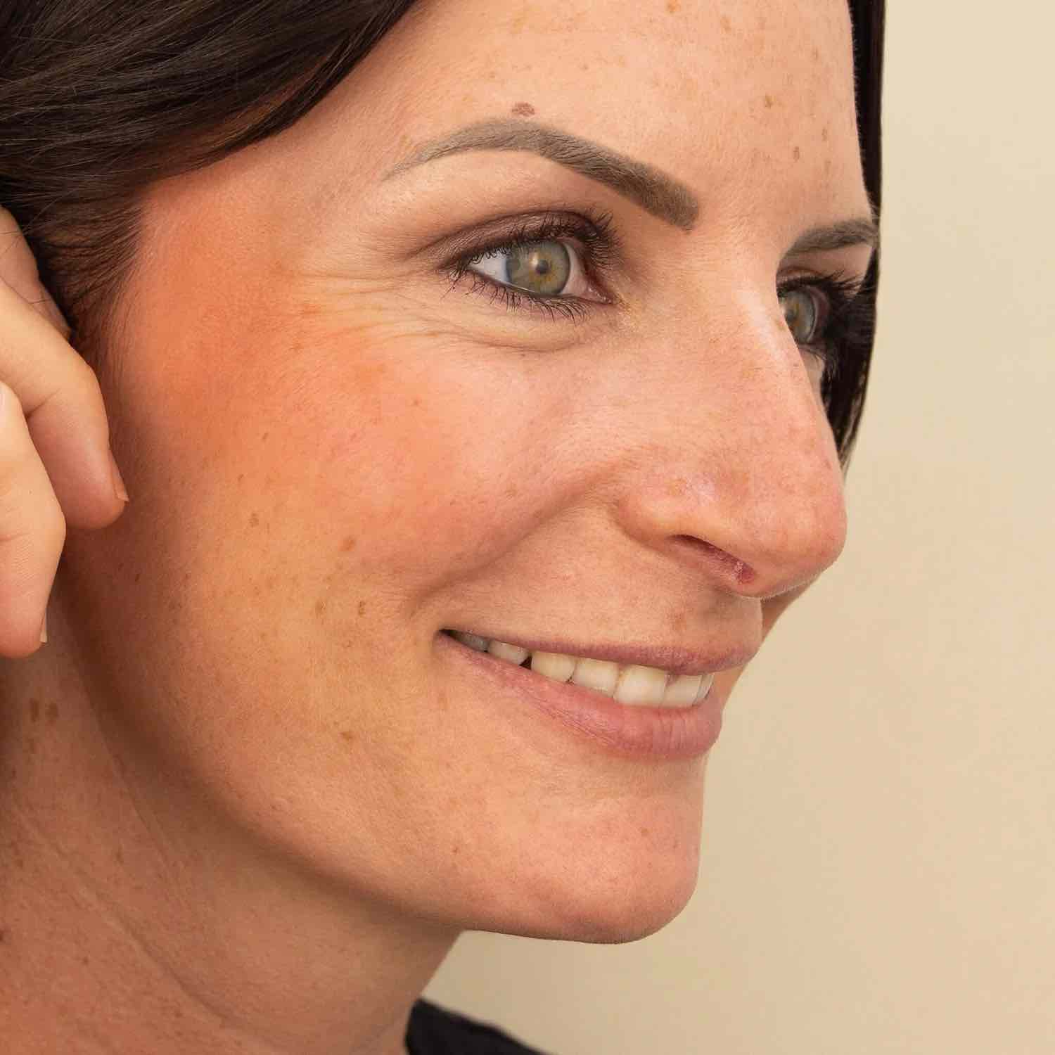 Un blush crème corail appliqué sur les joues d'une femme