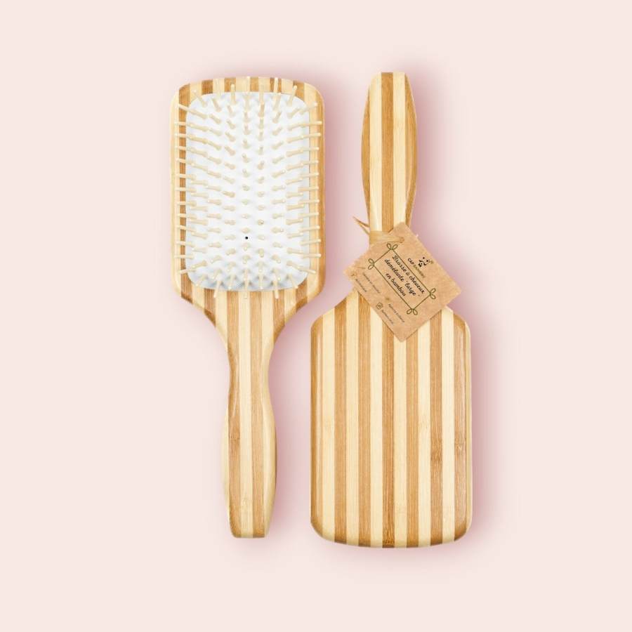 Une brosse à cheveux démêlante large de la marque Cap Bambou, sur un fond rose