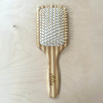 Une brosse à cheveux démêlante large de la marque Cap Bambou posée sur une table en bois