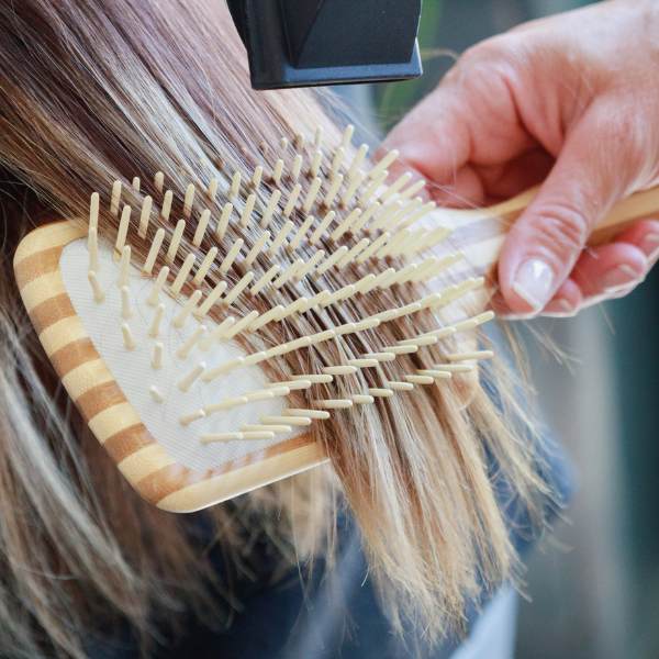 Une brosse à cheveux démêlante large de la marque Cap Bambou en train d'être utilisé sur des cheveux longs