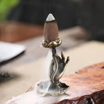 Un brûleur d'encens en cascade avec un cône allumé, la fumée s'écoulant doucement dans la main sculptée.