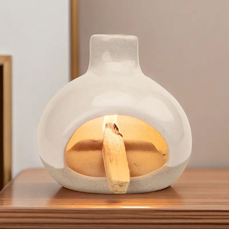 Un brûleur d'encens en céramique avec collecteur de cendres posé sur une table en bois, en fonctionnement avec un baton de palo santo allumé dedans