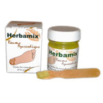 Un Baume Ayurvédique Herbamix pour les Pieds, Mains & Lèvres avec son emballage carton et une spatule en bois contenant un peu de baume sur le bout