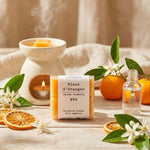 Un paquet de quatre carrés fondants Drake à la senteur Fleur d'Oranger devant un brule parfum et une orange
