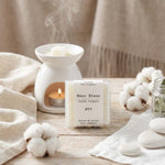 Un paquet de quatre carrés fondants Drake à la senteur Musc Blanc devant un brule parfum en céramique blanc
