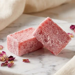 Carrés d'ambre fondants ByBazz rose bonbon sur marbre avec pétales roses séchés