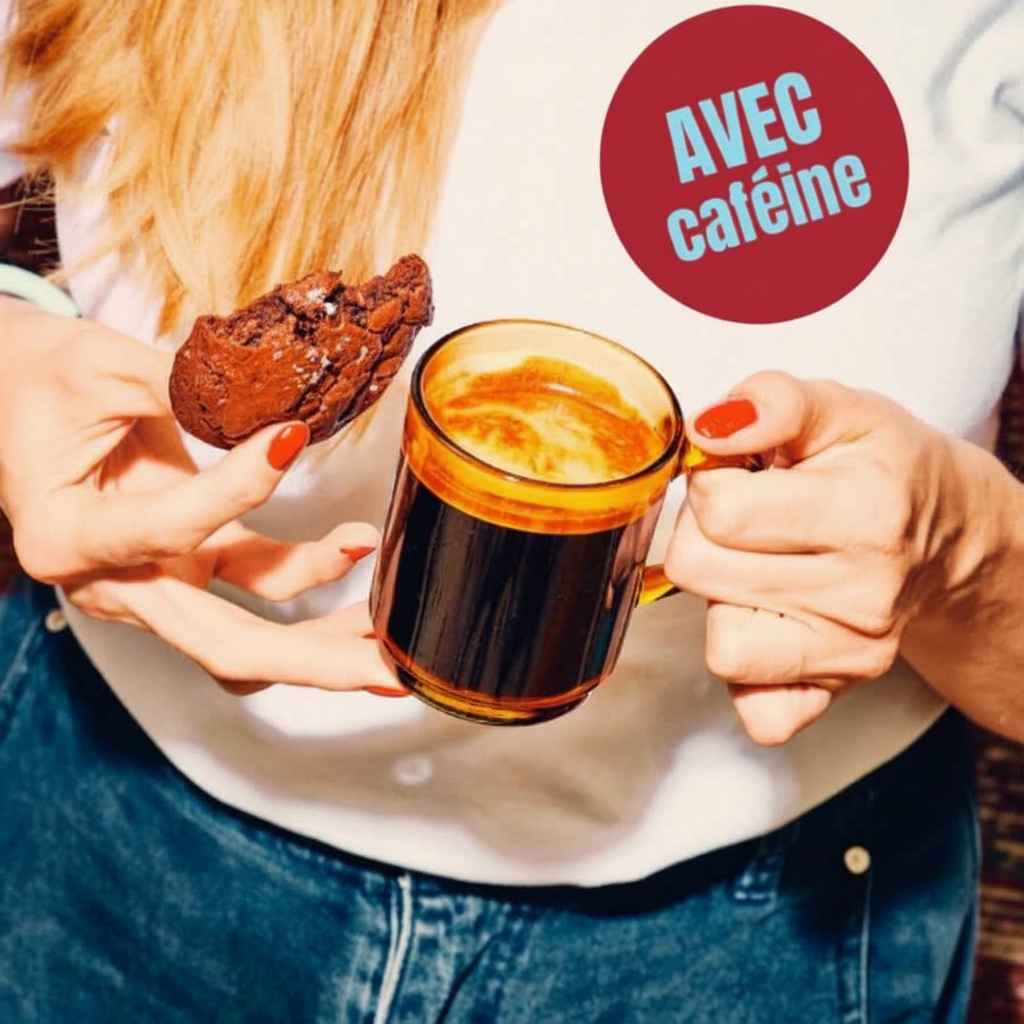 Une tasse de cagé chérico sans une main de femme accompagné d'une cookie gourmand.