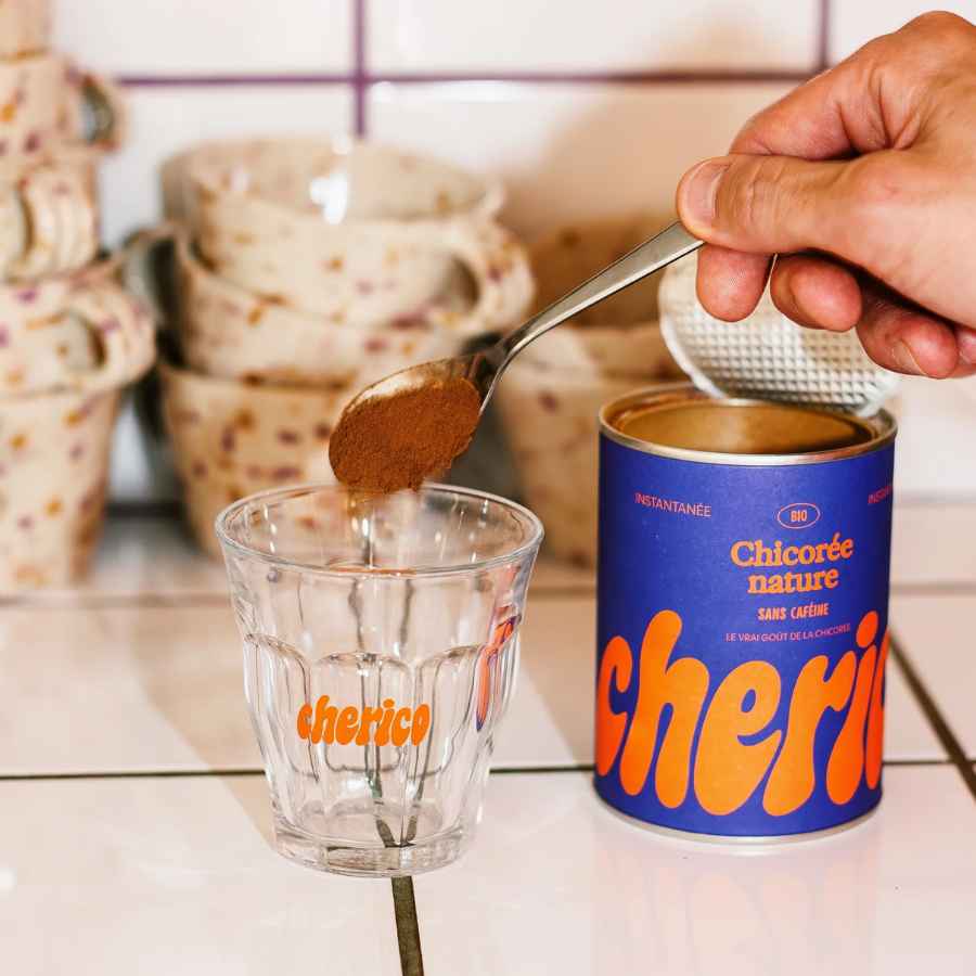 Une tasse de chicorée accompagné d'une boîte de chicorée sur un carrelage blanc.