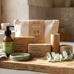 Coffret découverte Comme Avant : cinq produits sur une étagère de salle de bain en bois, près d'une coupelle en céramique verte et d'une serviette en lin