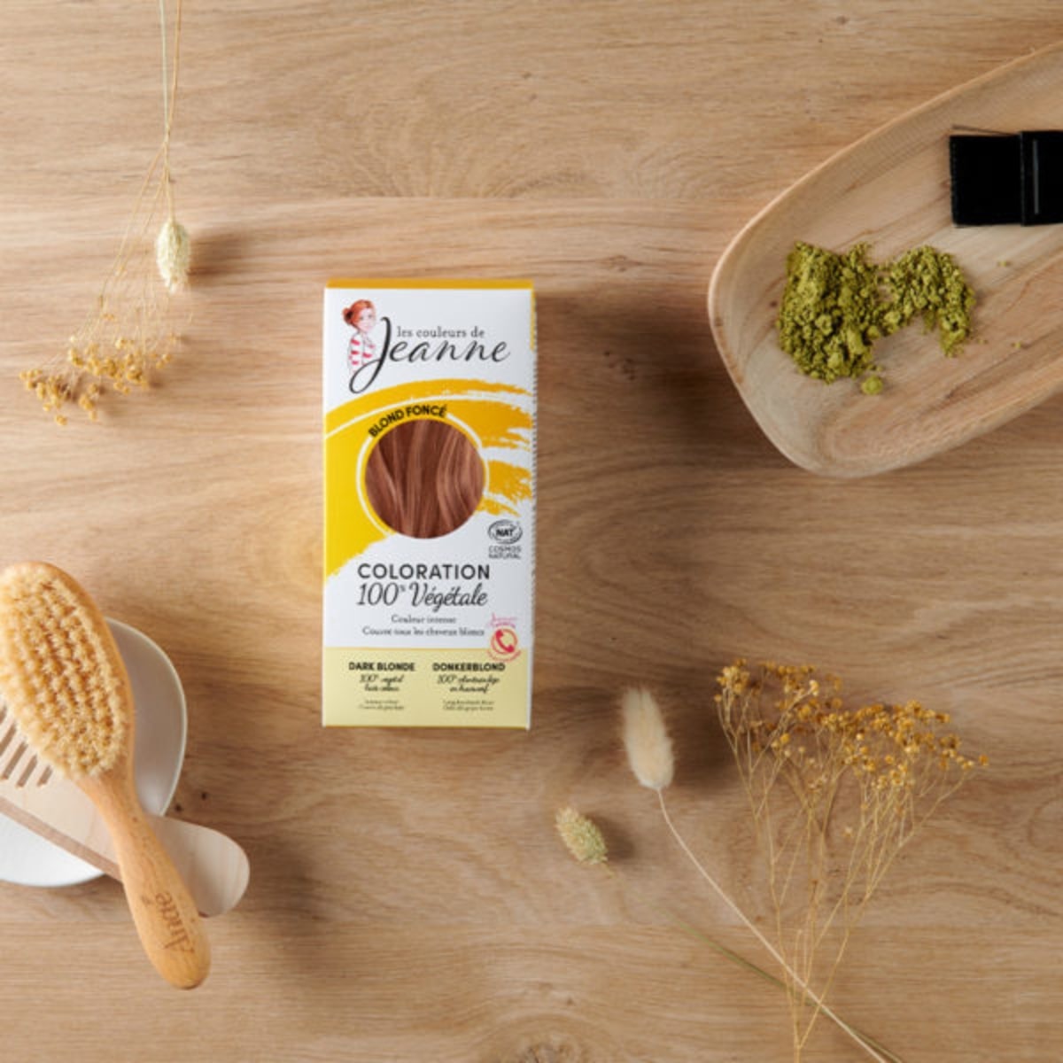 Une boîte de coloration blond foncé les couleurs de jeanne posé sur une table en bois avec des accessoires un peigne et une brosse