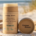 Crème solaire minérale solide SPF50 Comme Avant avec packaging bois sur plage ensoleillée