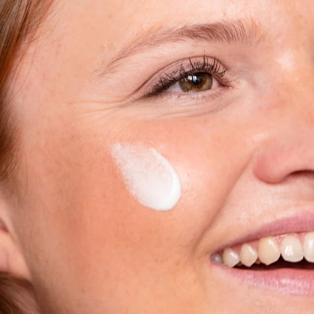 Un visage de femme avec une goutte de crème hydratante sur la joue