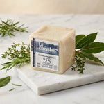 Cube de savon de Marseille La Corvette 300g sur marbre blanc avec herbes fraîches