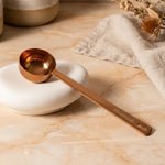 Cuillère doseuse Pimpant rose gold sur plat blanc, style minimaliste élégant