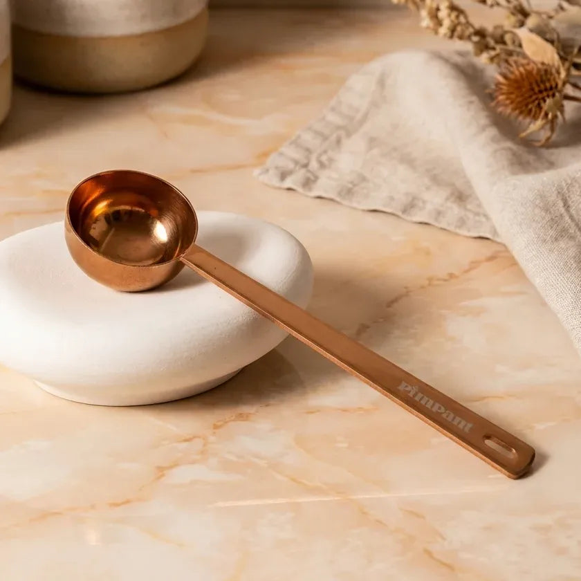 Cuillère doseuse Pimpant rose gold sur plat blanc, style minimaliste élégant